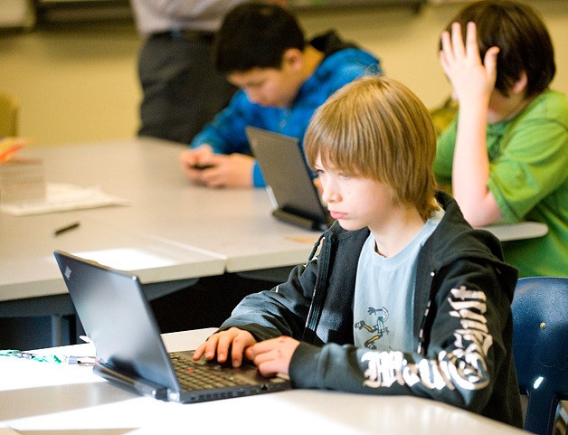 Ciabhan Moore works at a laptop at the district’s Big Picture school. In background are Oscar Zeng
