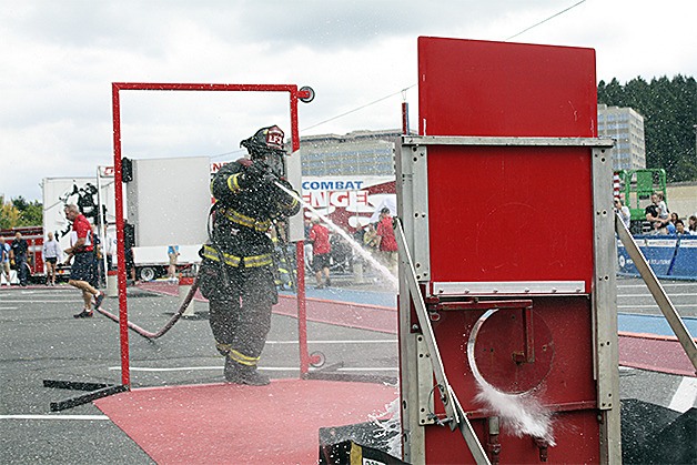 A firefigher in full gear shoots a target with a fire hose he has just dragged 75 feet.