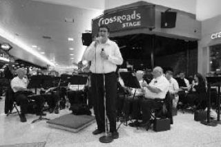 The Bellevue Community Band conductor Philip Donley speaks to the crowd gathered to hear the music at Crossroads