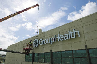 A worker from TubeArt Architectural & Electrical Displays in Seattle positions the Group Health insignia on the company’s sign at its new facility in Bellevue’s hospital district.