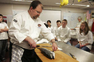 Rover’s Chef de Cuisine Adam Hoffman fillets a farm-raised salmon as Newport High School culinary students watch.