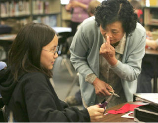 Chinese paper cutting artist/kindergarten educator Yao Bingyue suggests to Tillicum Middle School student Kayla Chan to make a tiny slit to make a nose on the apple