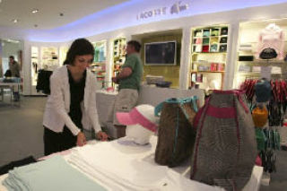 Lacoste store manager Shiloh Rodgers fixes the shirts on display as customers look around the new store.
