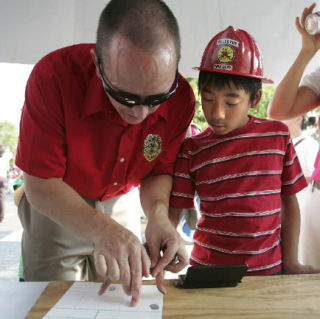 Chi-Nhan Vo gets fingerprinted with help from Mike Wolters during National Night Out at the Crossroads Police Station on Tuesday