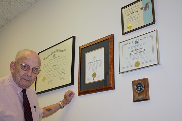 John McGaw stands in front of various awards he received during his time as scoutmaster in Bellevue. The awards hang in his office.
