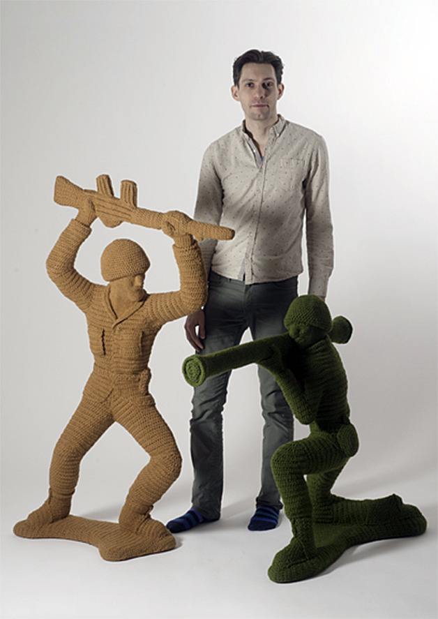 Artist Nathan Vincent stands with two of his yarn soldiers
