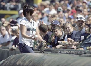 Mariners’ ball girl Erin Tsutsumoto hands out a ball that she caught after it rolled over to right field