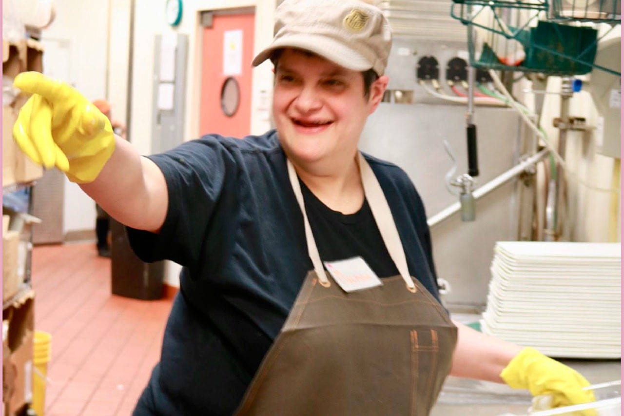 Maslan joyfully greets a co-worker as she washes dishes at work at an Issaquah restaurant where she has worked for over six years. Photo courtesy of Regina Friedland