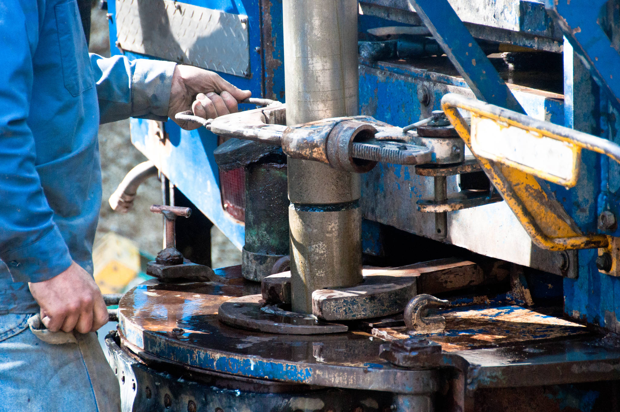 A worker uses a large wrench to screw on a drill casing during the operation of a water well drill rig. Photo by Erika Mitchell