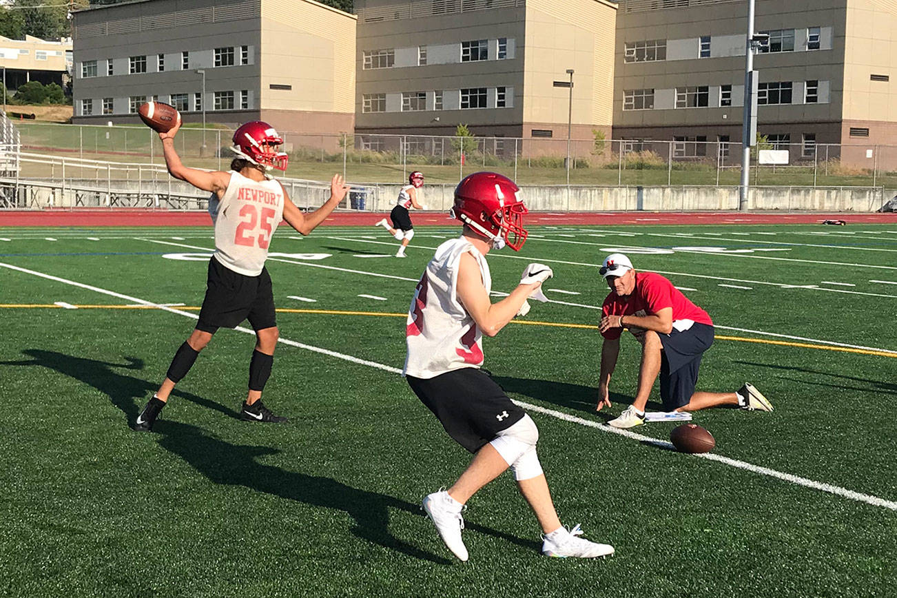 Newport Knights quarterback Tre Louis, left, throws a seam route to a wide receiver during an evening practice session on Aug. 17 at Newport High School in Factoria. Knights head coach Drew Oliver, right, snapped Louis the ball on the play. Shaun Scott/staff photo