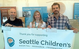 Georgetown Brewing Sales Manager Mat Connolly (left) and  Tap House Grill owner Paul Reder (right) present  Katie Fath from Seattle Children’s Hospital a check for $1
