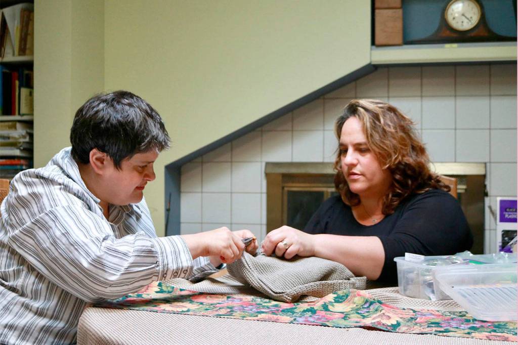 Listening intently to her sister Michelle&rsquo;s patient instructions, they work together to fix the broken zipper pull on her purse. Maslan is focused on their task in the family&rsquo;s Bellevue home. Photo courtesy of Regina Friedland
