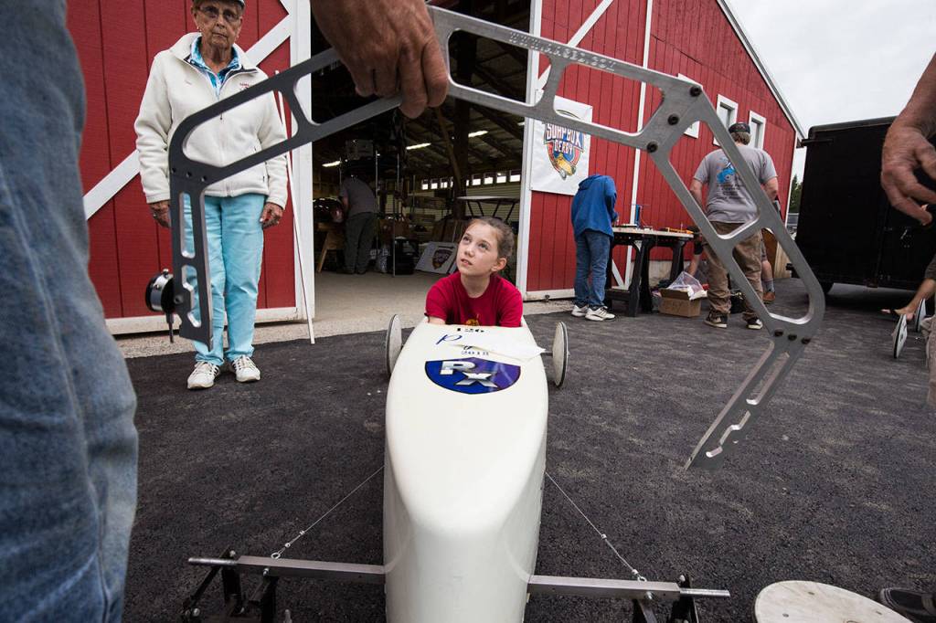 Peyton Calkins listens as adults talk about the bend in a rod that keeps the wheels straight under pressure from the drivers weight in a soap box derby car. (Andy Bronson / The Herald)