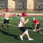 Newport Knights quarterback Tre Louis, left, throws a seam route to a wide receiver during an evening practice session on Aug. 17 at Newport High School in Factoria. Knights head coach Drew Oliver, right, snapped Louis the ball on the play. Shaun Scott/staff photo